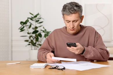 Photo of Man paying bills with smartphone at wooden table indoors. Space for text