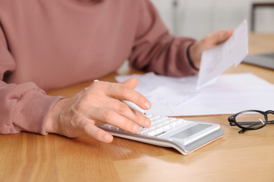 Photo of Paying bills. Man with different invoices using calculator at wooden table indoors, closeup