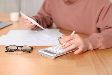 Photo of Paying bills. Man with different invoices using calculator at wooden table indoors, closeup