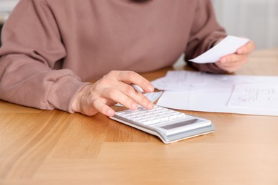 Photo of Paying bills. Man with different invoices using calculator at wooden table indoors, closeup