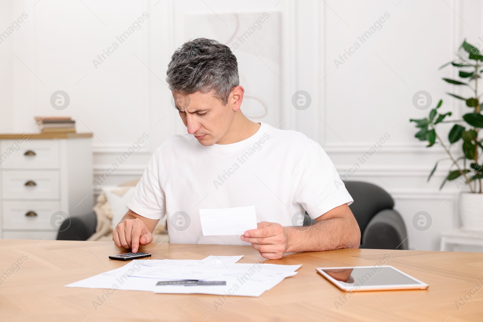 Photo of Paying bills. Man with different invoices using calculator at wooden table indoors