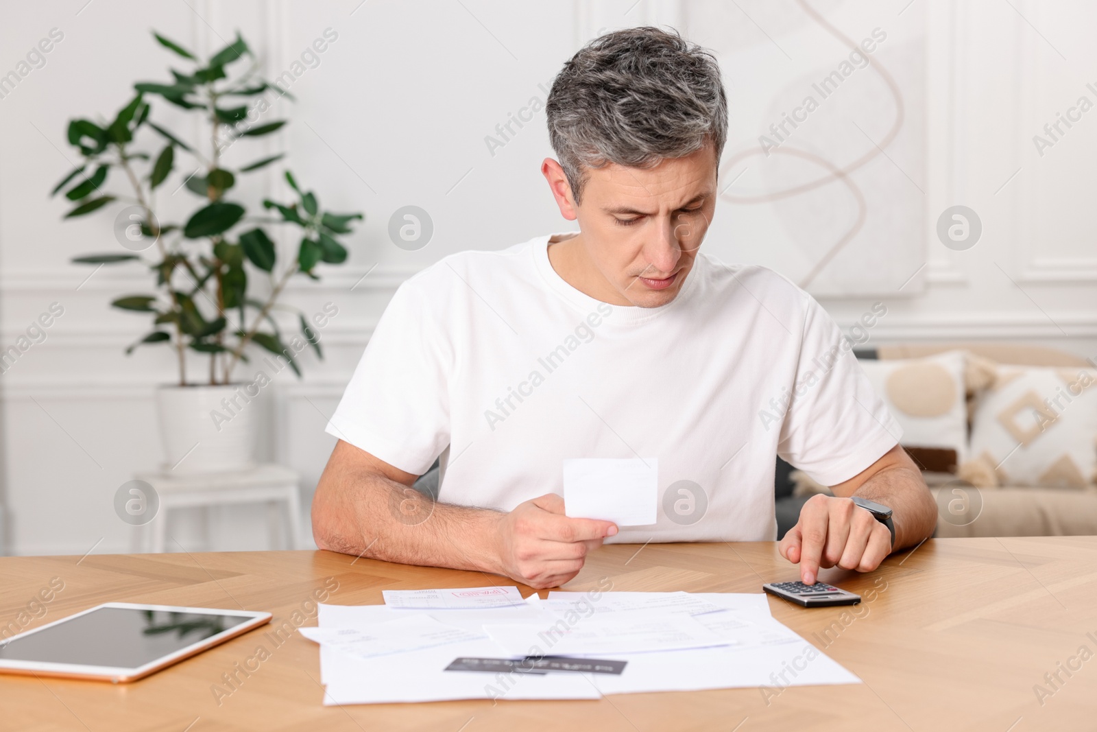 Photo of Paying bills. Man with different invoices using calculator at wooden table indoors