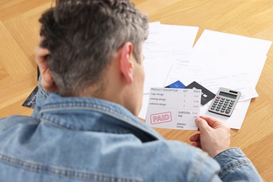 Photo of Paying bills. Man with reviewing invoices at wooden table, above view