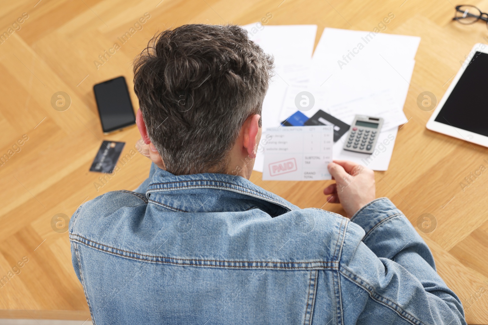 Photo of Paying bills. Man with reviewing invoices at wooden table, above view