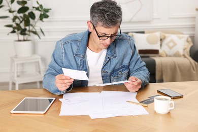 Photo of Paying bills. Man with reviewing invoices at wooden table indoors