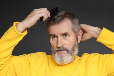 Photo of Handsome man combing his hair on dark grey background