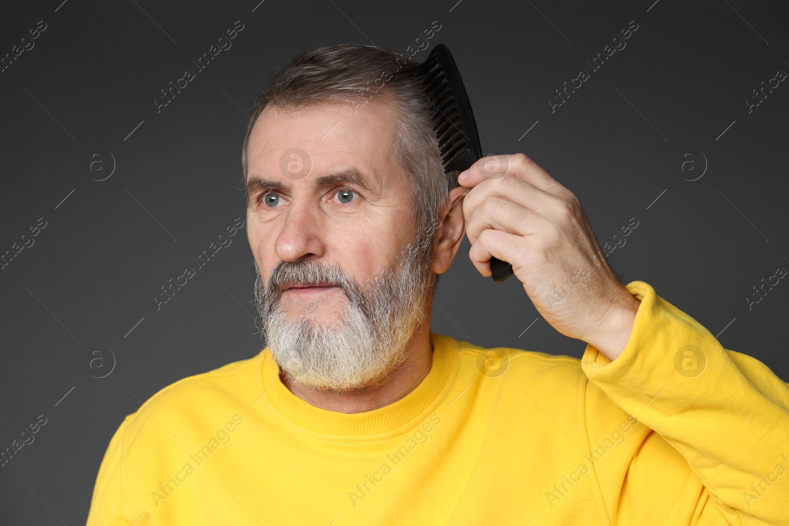 Photo of Handsome man combing his hair on dark grey background