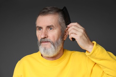 Photo of Handsome man combing his hair on dark grey background