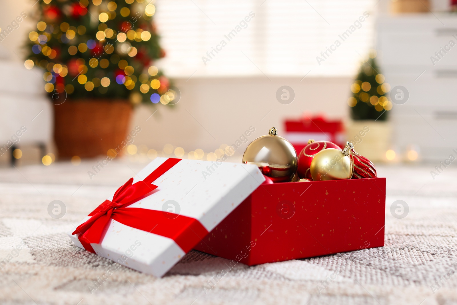 Photo of Christmas gift box with baubles on floor indoors, closeup