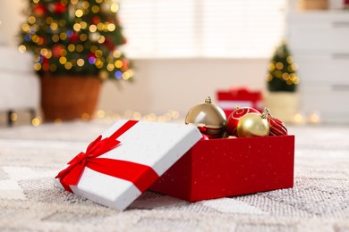 Photo of Christmas gift box with baubles on floor indoors, closeup