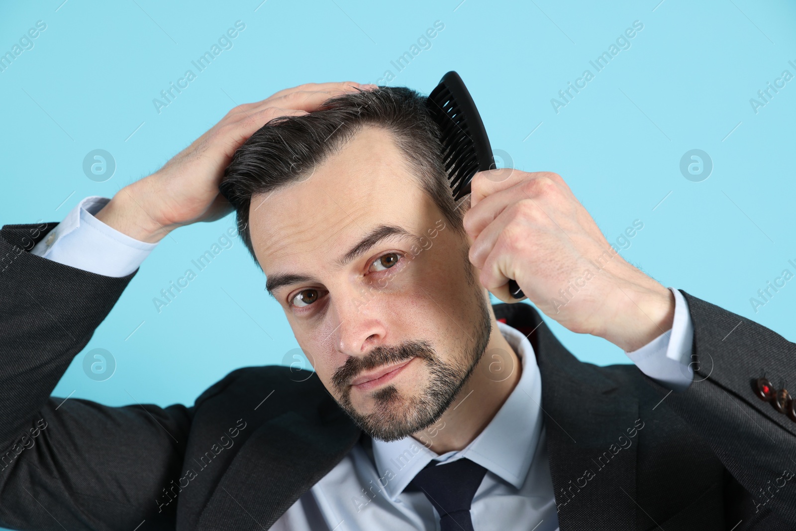 Photo of Handsome man stylish his hair with comb on light blue background