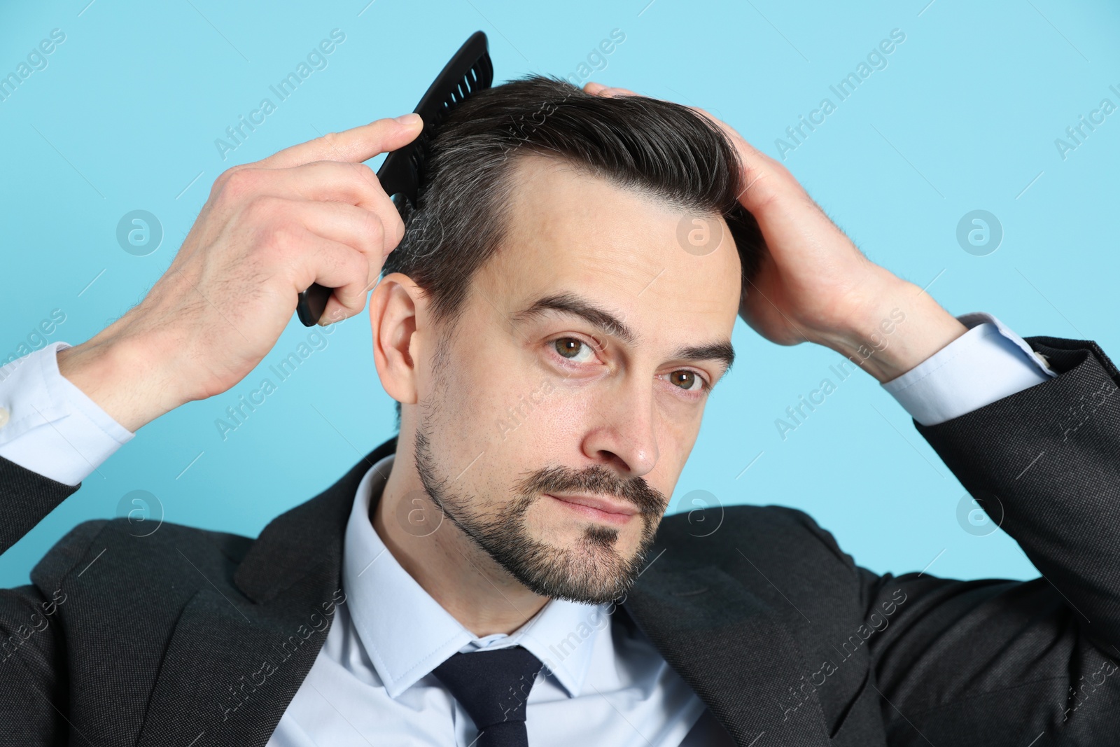 Photo of Handsome man stylish his hair with comb on light blue background