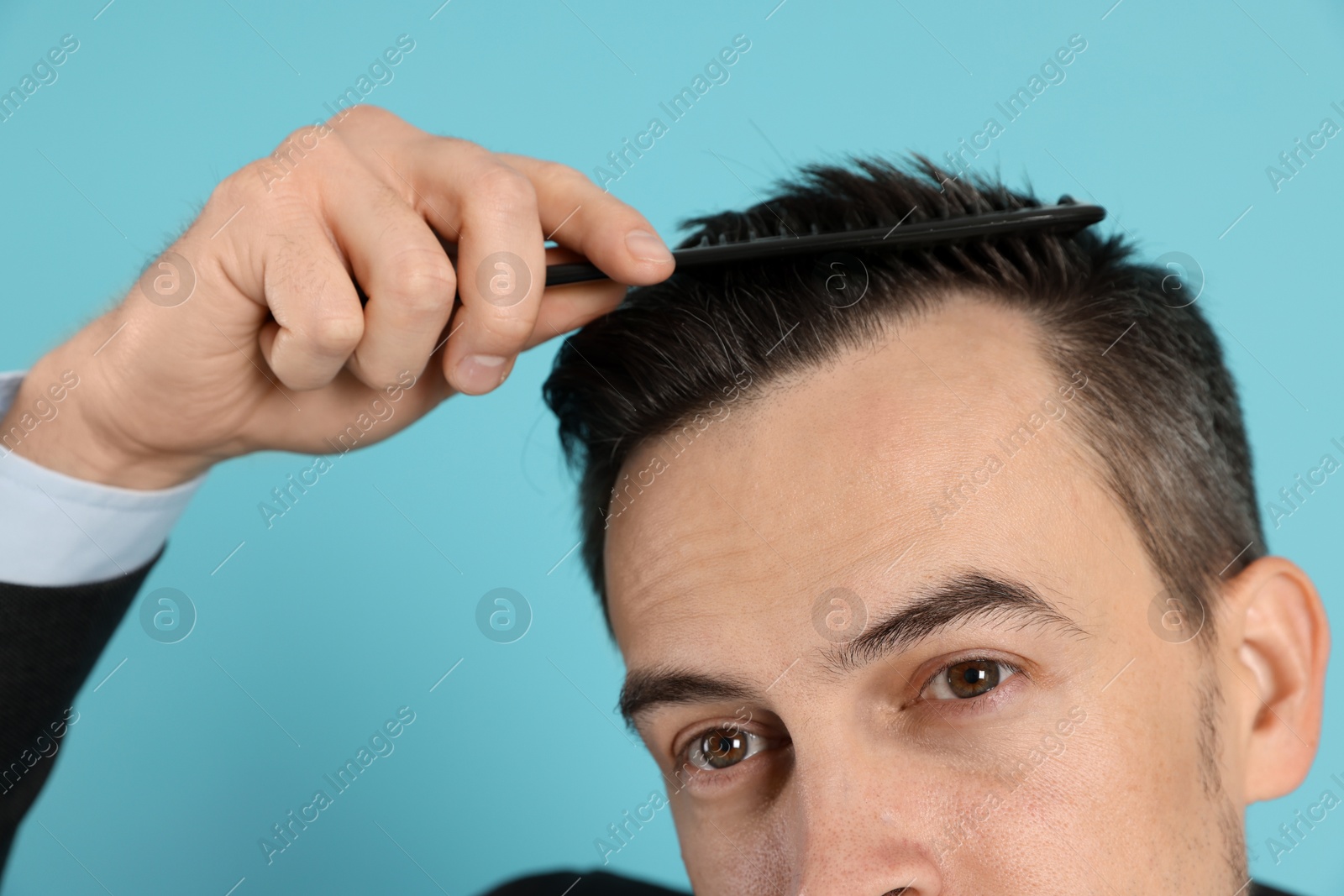 Photo of Handsome man stylish his hair with comb on light blue background, closeup