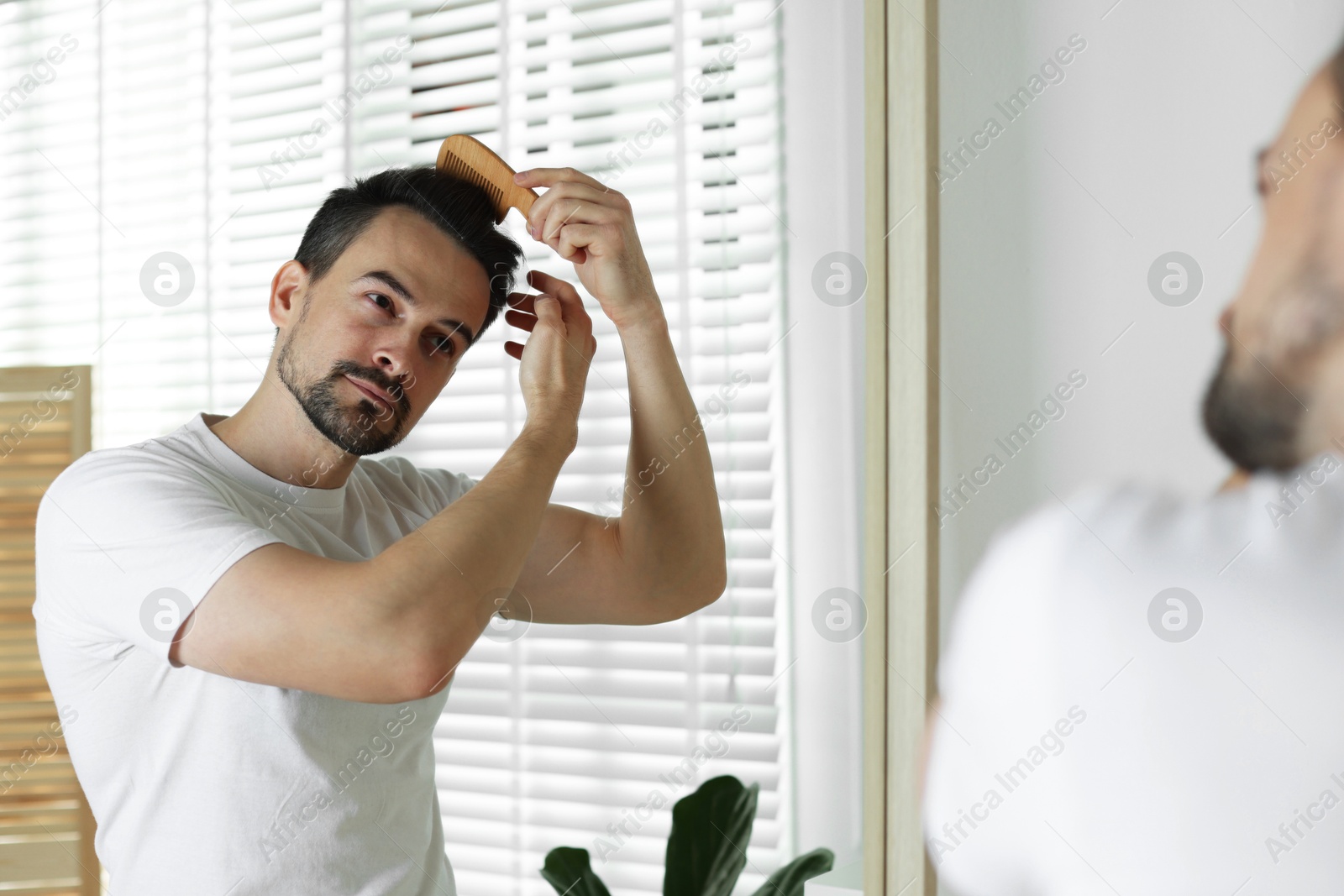 Photo of Handsome man styling his hair with comb near mirror at home