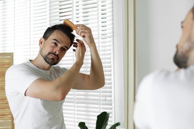 Handsome man styling his hair with comb near mirror at home