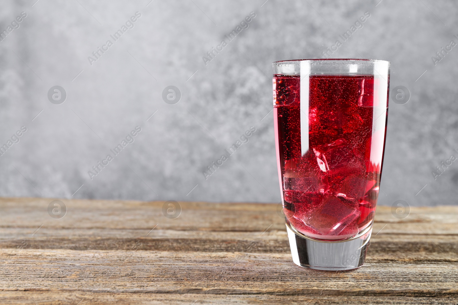 Photo of Sweet soda water with ice cubes in glass on wooden table, space for text