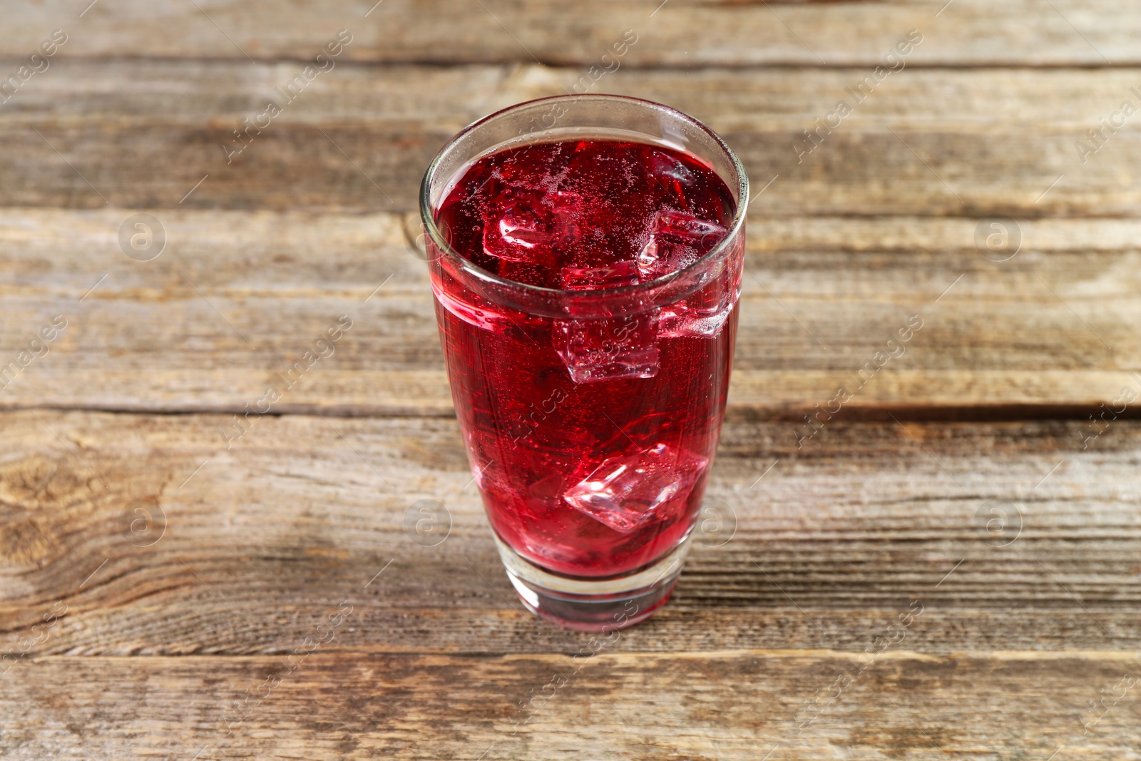 Photo of Sweet soda water with ice cubes in glass on wooden table, closeup