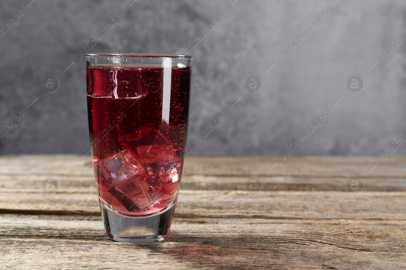 Sweet soda water with ice cubes in glass on wooden table, space for text Photo of Sweet soda water with ice cubes in glass on wooden table, space for text