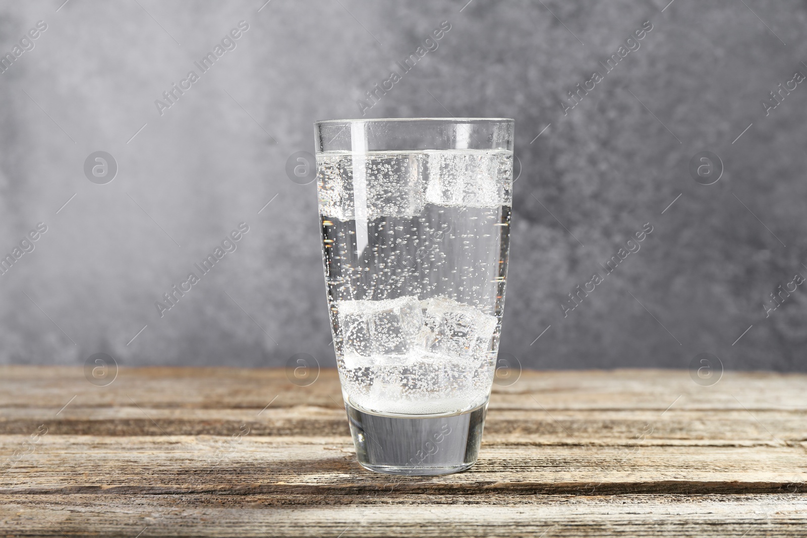 Photo of Soda water with ice cubes in glass on wooden table