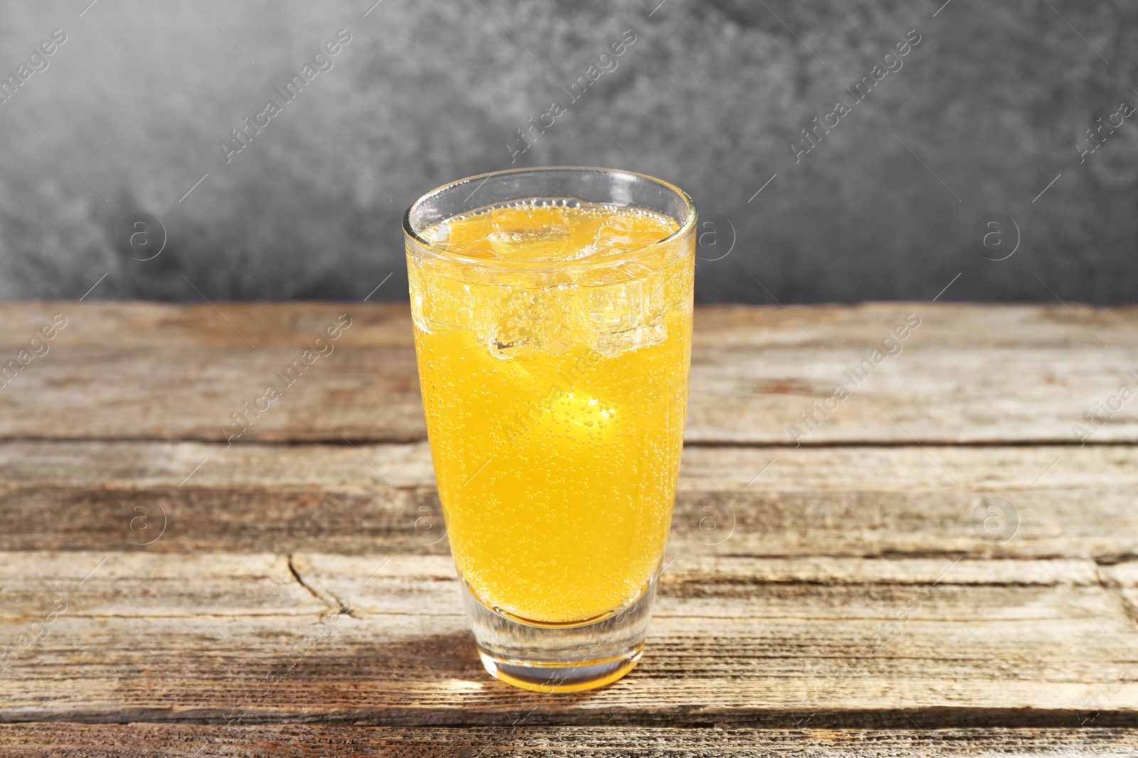 Photo of Sweet soda water with ice cubes in glass on wooden table, closeup