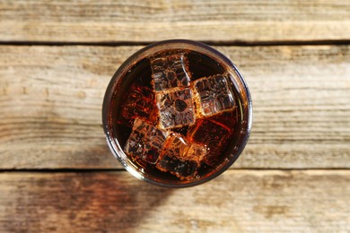 Photo of Sweet soda water with ice cubes in glass on wooden table, top view