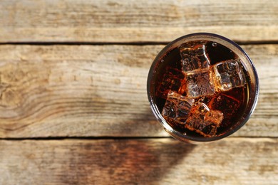 Photo of Sweet soda water with ice cubes in glass on wooden table, top view. Space for text