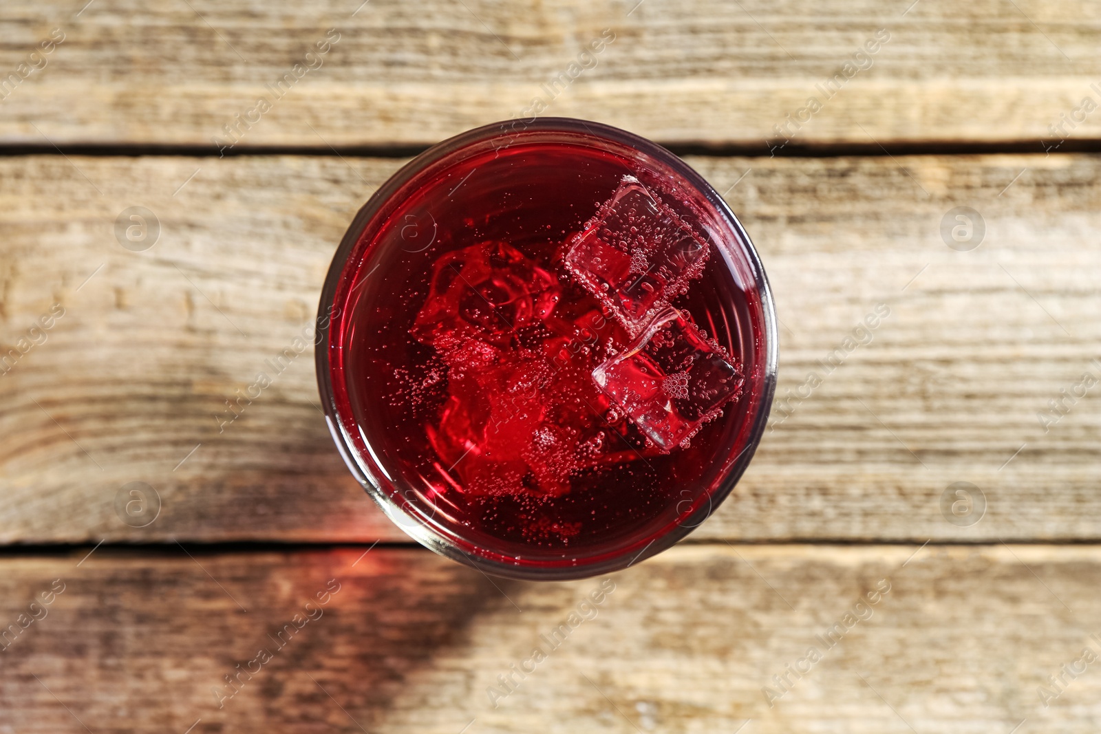 Photo of Sweet soda water with ice cubes in glass on wooden table, top view