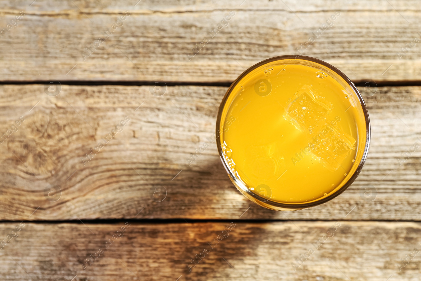 Photo of Sweet soda water with ice cubes in glass on wooden table, top view. Space for text