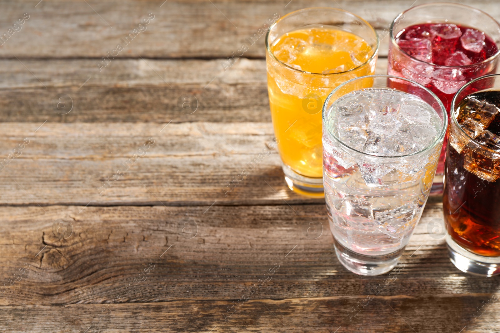 Photo of Soda water of different flavors with ice cubes in glasses on wooden table, closeup. Space for text