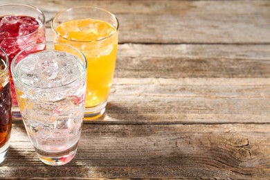 Photo of Soda water of different flavors with ice cubes in glasses on wooden table, closeup. Space for text