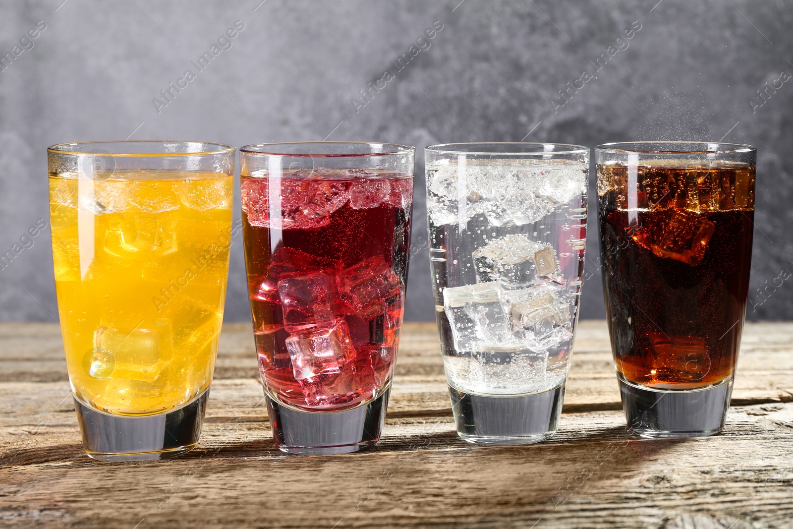 Photo of Soda water of different flavors with ice cubes in glasses on wooden table