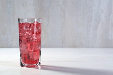 Photo of Sweet soda water with ice cubes in glass on white wooden table, space for text