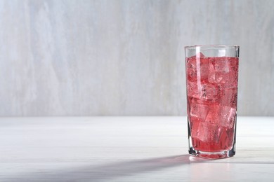 Photo of Sweet soda water with ice cubes in glass on white wooden table, space for text