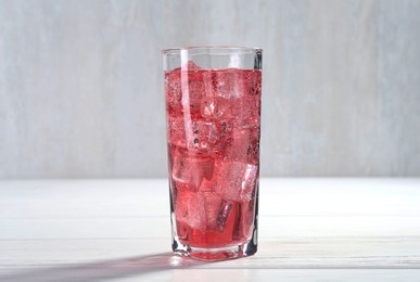 Photo of Sweet soda water with ice cubes in glass on white wooden table, closeup