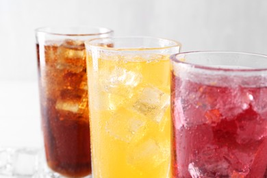 Photo of Soda water of different flavors with ice cubes in glasses on white table, closeup