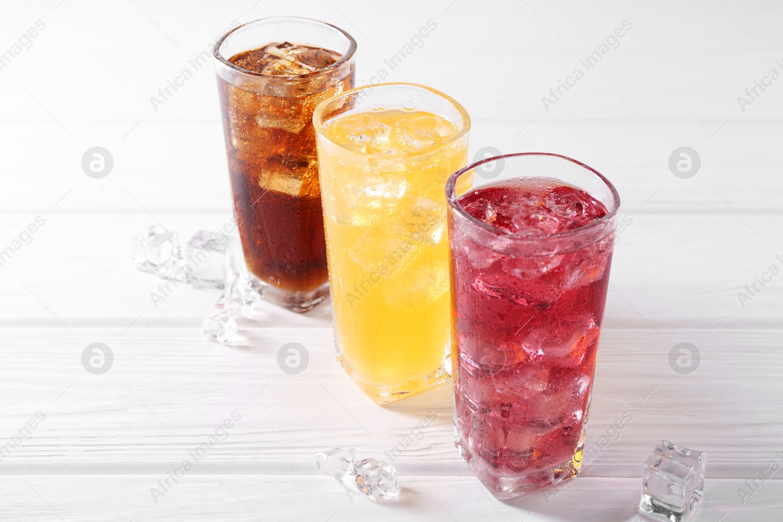 Photo of Soda water of different flavors in glasses with ice cubes on white wooden table