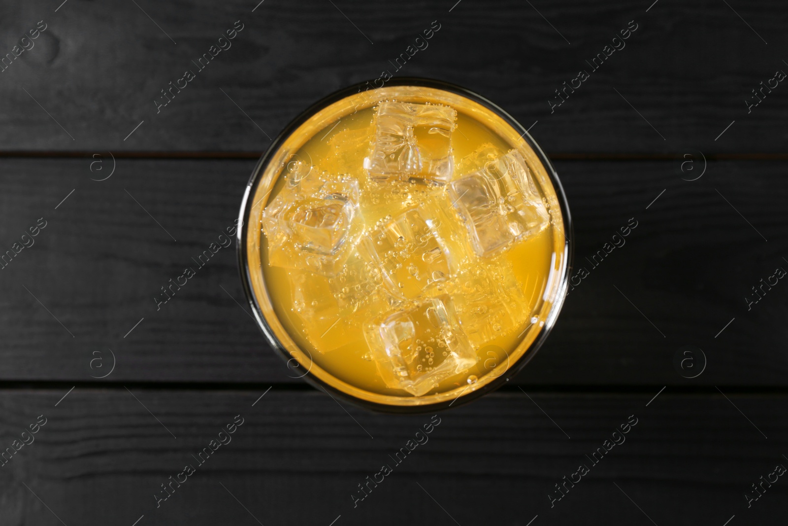 Photo of Sweet soda water with ice cubes in glass on black wooden table, top view