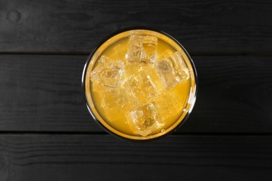 Photo of Sweet soda water with ice cubes in glass on black wooden table, top view