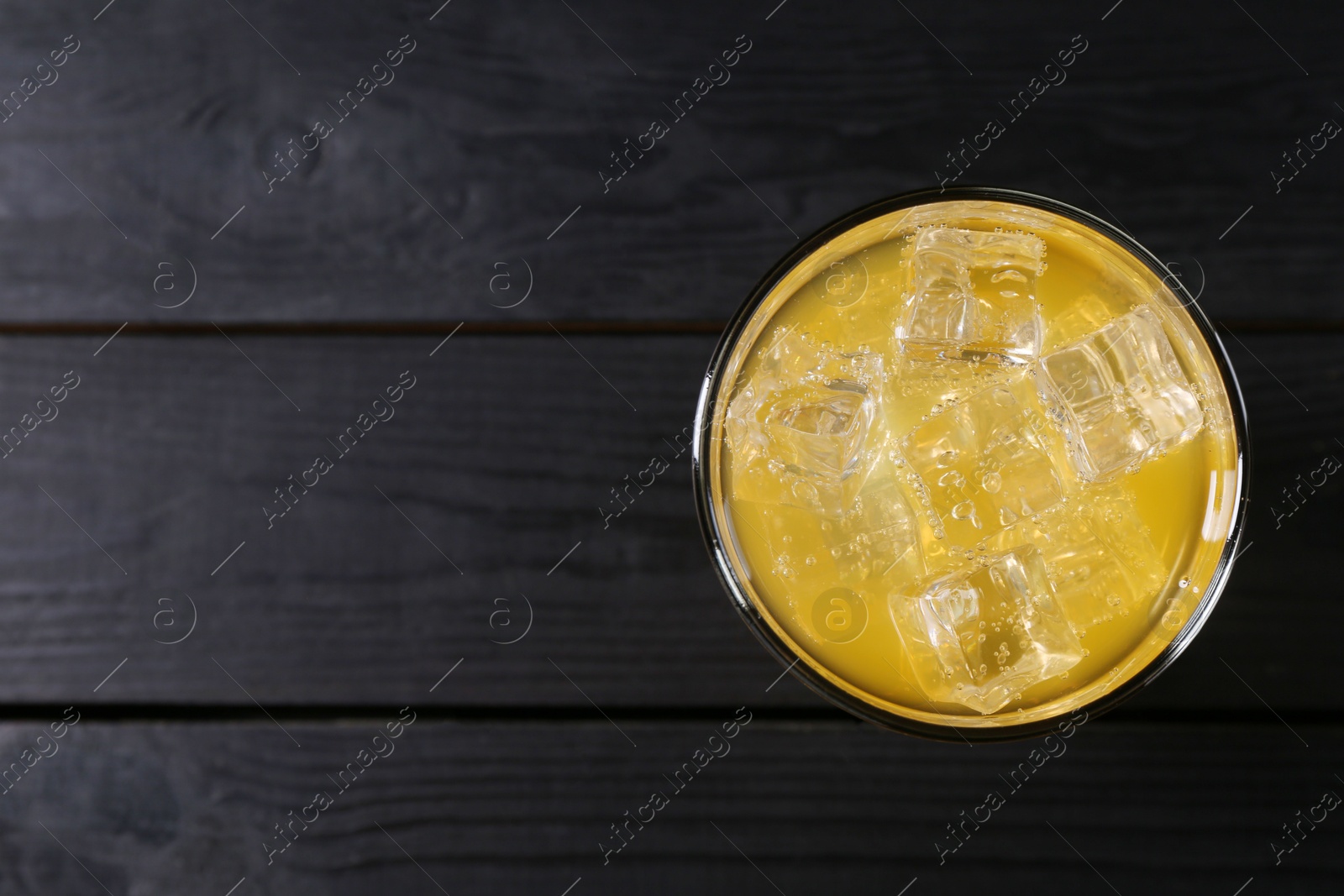 Photo of Sweet soda water with ice cubes in glass on black wooden table, top view. Space for text