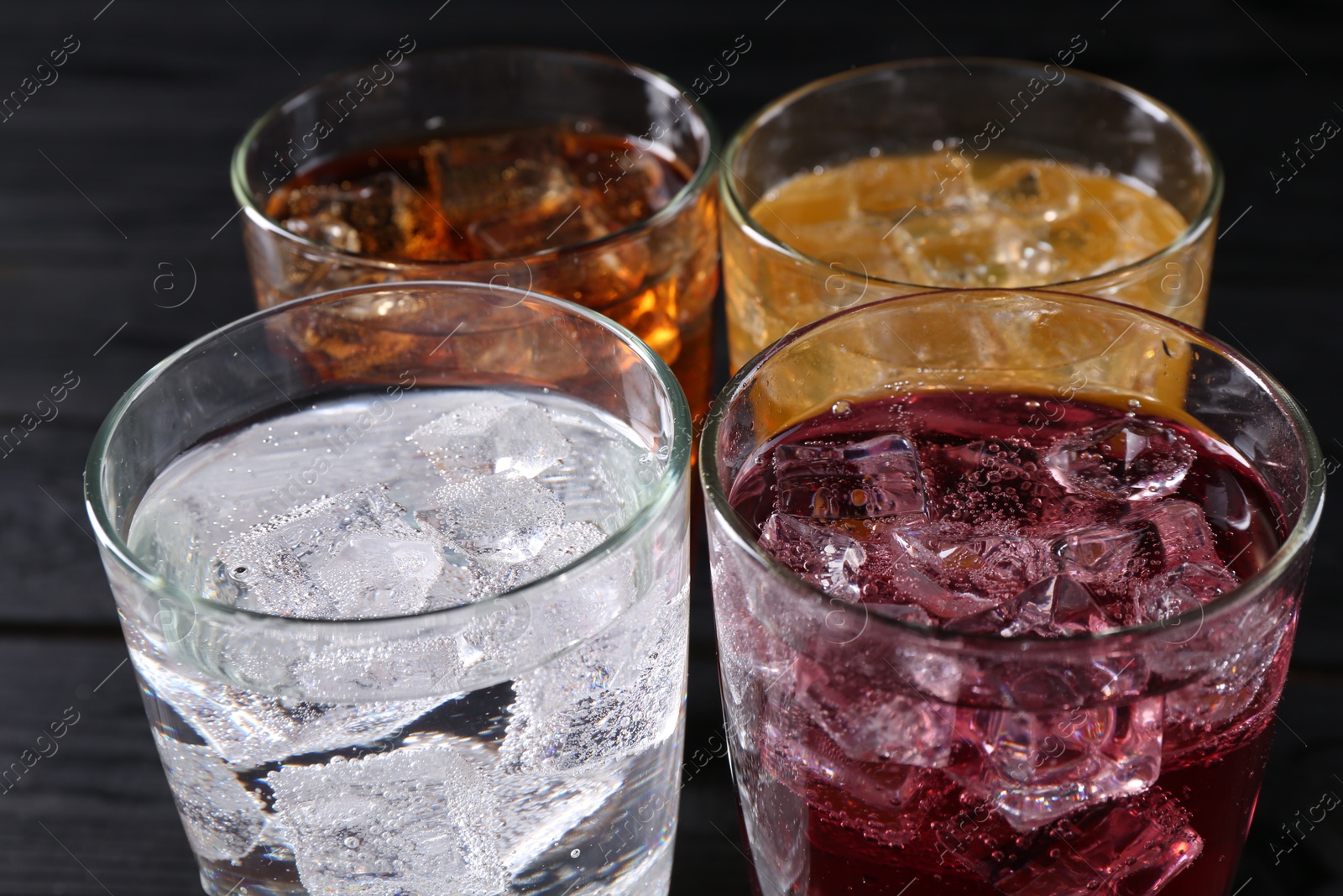 Photo of Refreshing soda water of different flavors with ice cubes in glasses on table, closeup