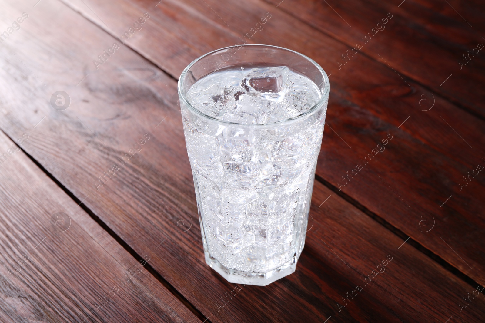 Photo of Refreshing soda water with ice cubes in glass on wooden table