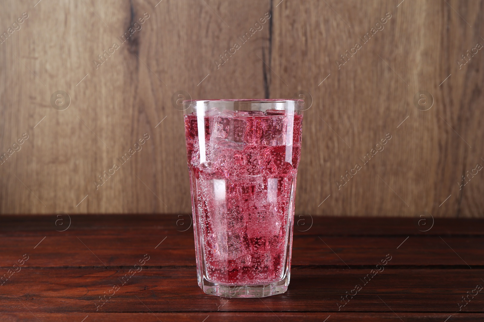 Photo of Sweet soda water with ice cubes in glass on wooden table