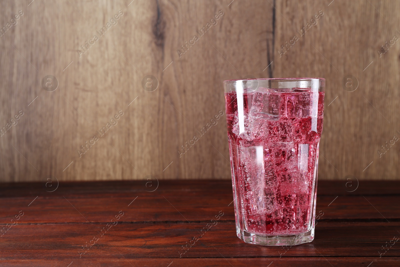 Photo of Sweet soda water with ice cubes in glass on wooden table, space for text