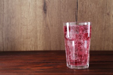 Photo of Sweet soda water with ice cubes in glass on wooden table, space for text