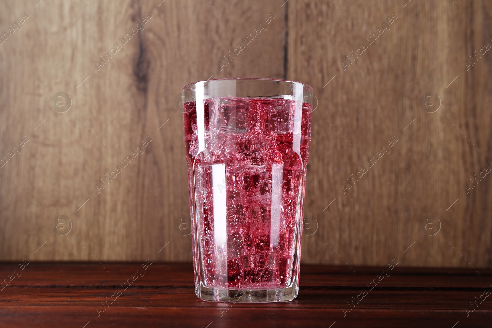 Photo of Sweet soda water with ice cubes in glass on wooden table