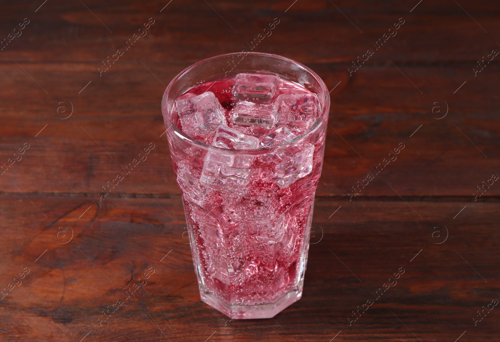 Photo of Sweet soda water with ice cubes in glass on wooden table