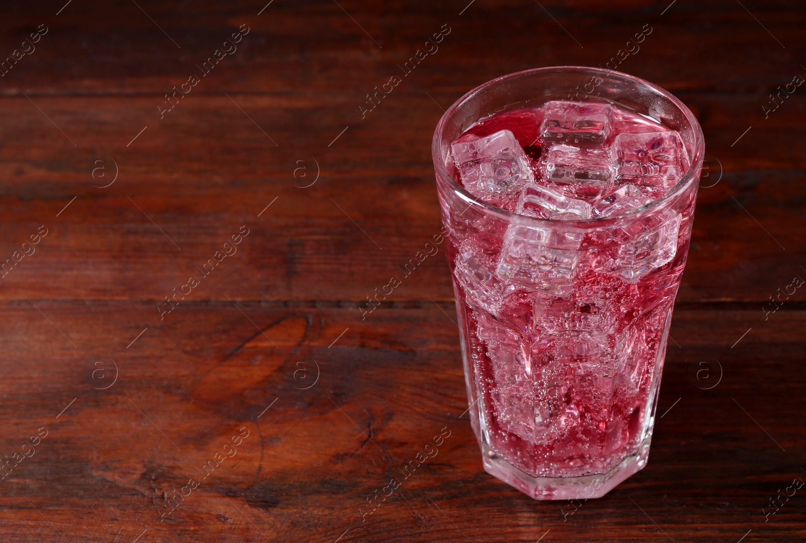 Photo of Sweet soda water with ice cubes in glass on wooden table, space for text