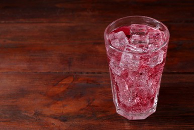 Photo of Sweet soda water with ice cubes in glass on wooden table, space for text