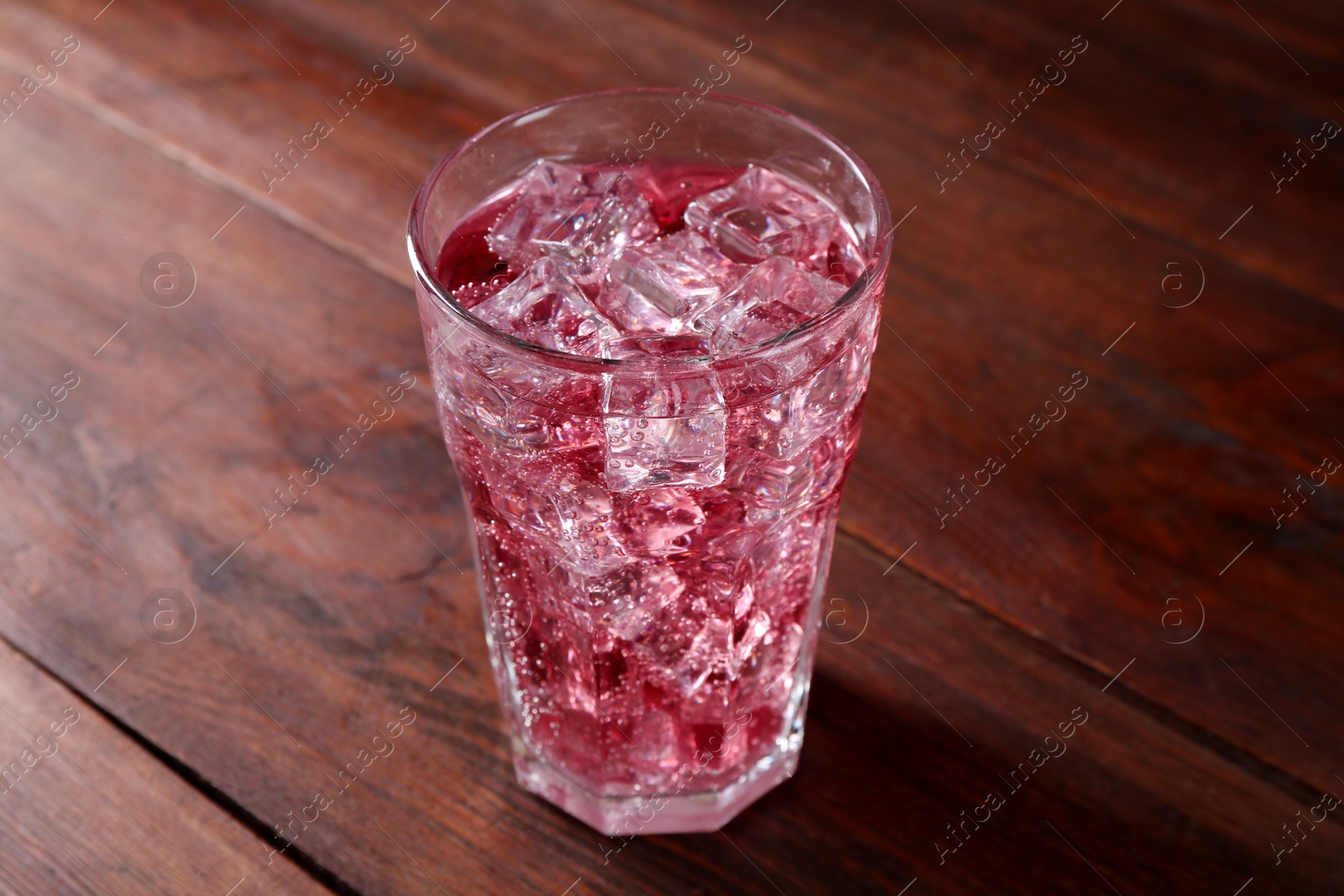 Photo of Sweet soda water with ice cubes in glass on wooden table, closeup