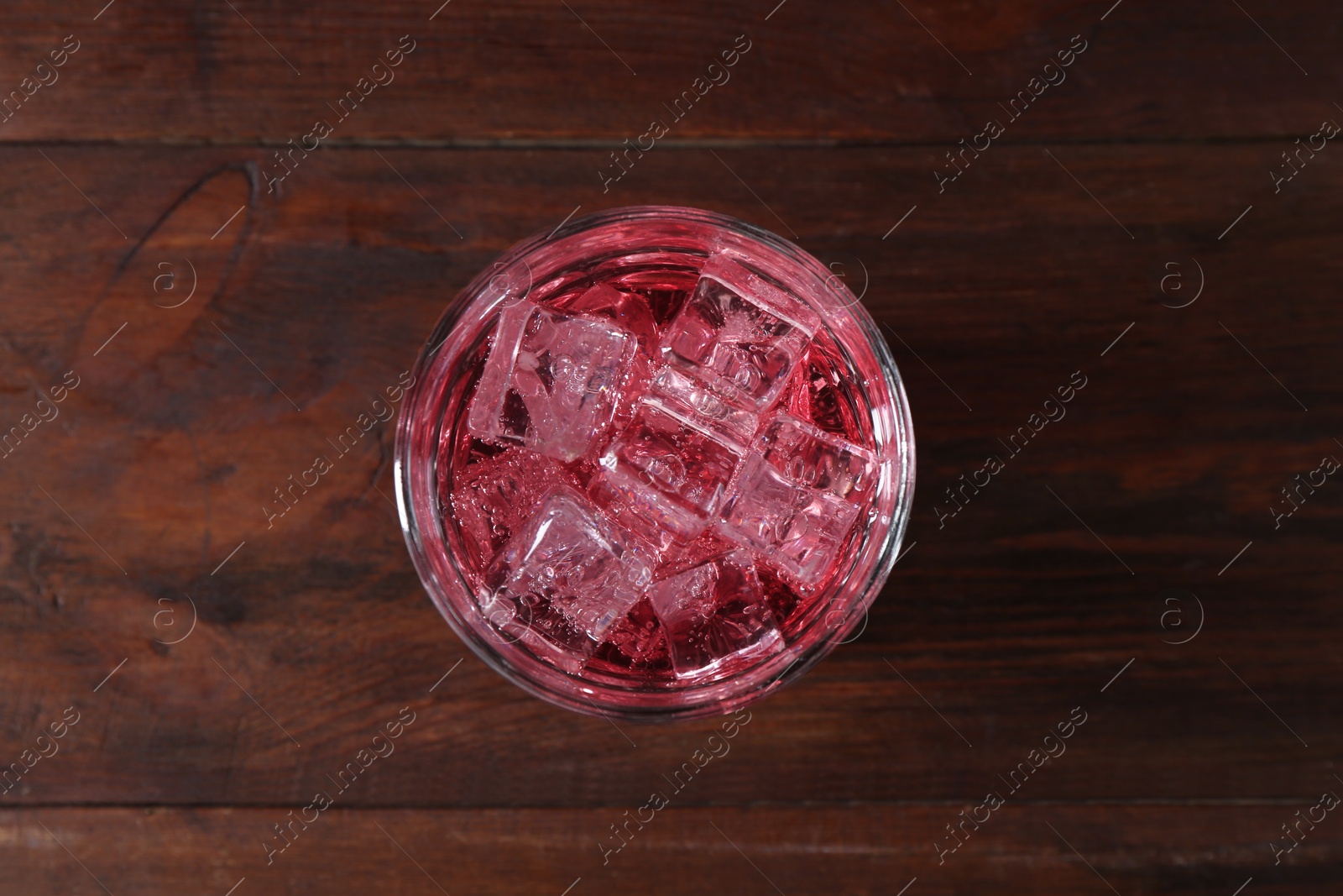 Photo of Sweet soda water with ice cubes in glass on wooden table, top view